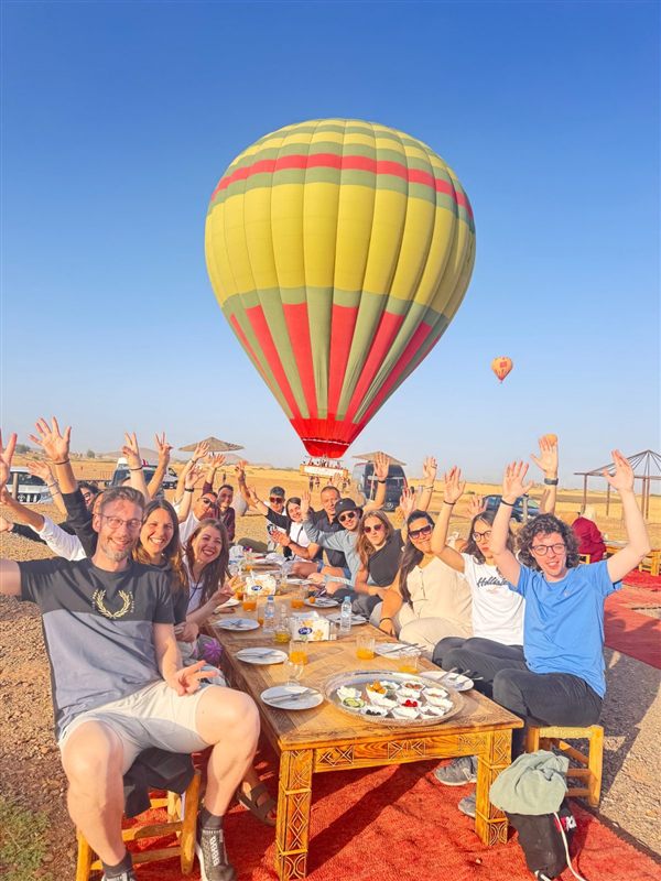 Gruppo di viaggiatori felici a colazione con una mongolfiera gialla dietro a Marrakech