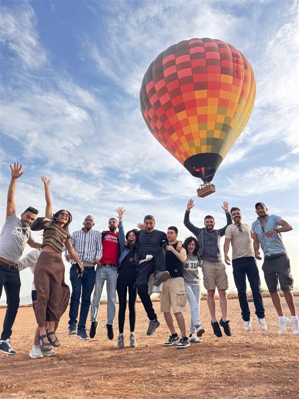 Gruppo di viaggiatori che saltano di gioia davanti a una mongolfiera colorata