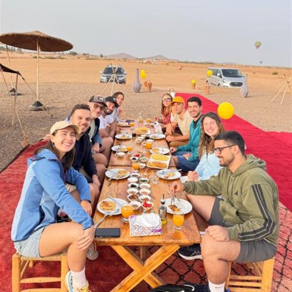 Gruppo di viaggiatori sorridenti alla lunga tavola della colazione nel campo, con le mongolfiere sullo sfondo
