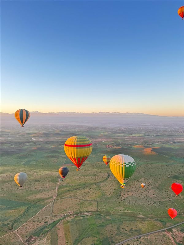 Mongolfiere che volano sopra i campi con l'Atlante sullo sfondo all'alba