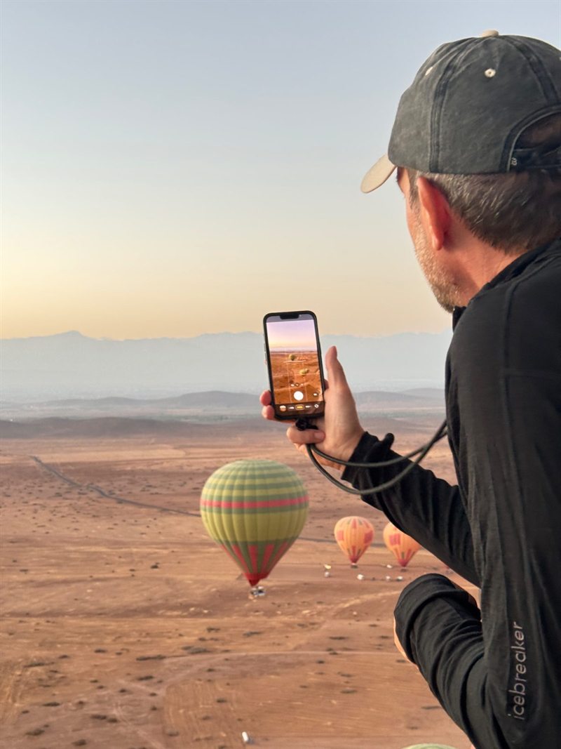 Viaggiatore che fotografa con il cellulare le mongolfiere sopra il deserto di pietra all’alba